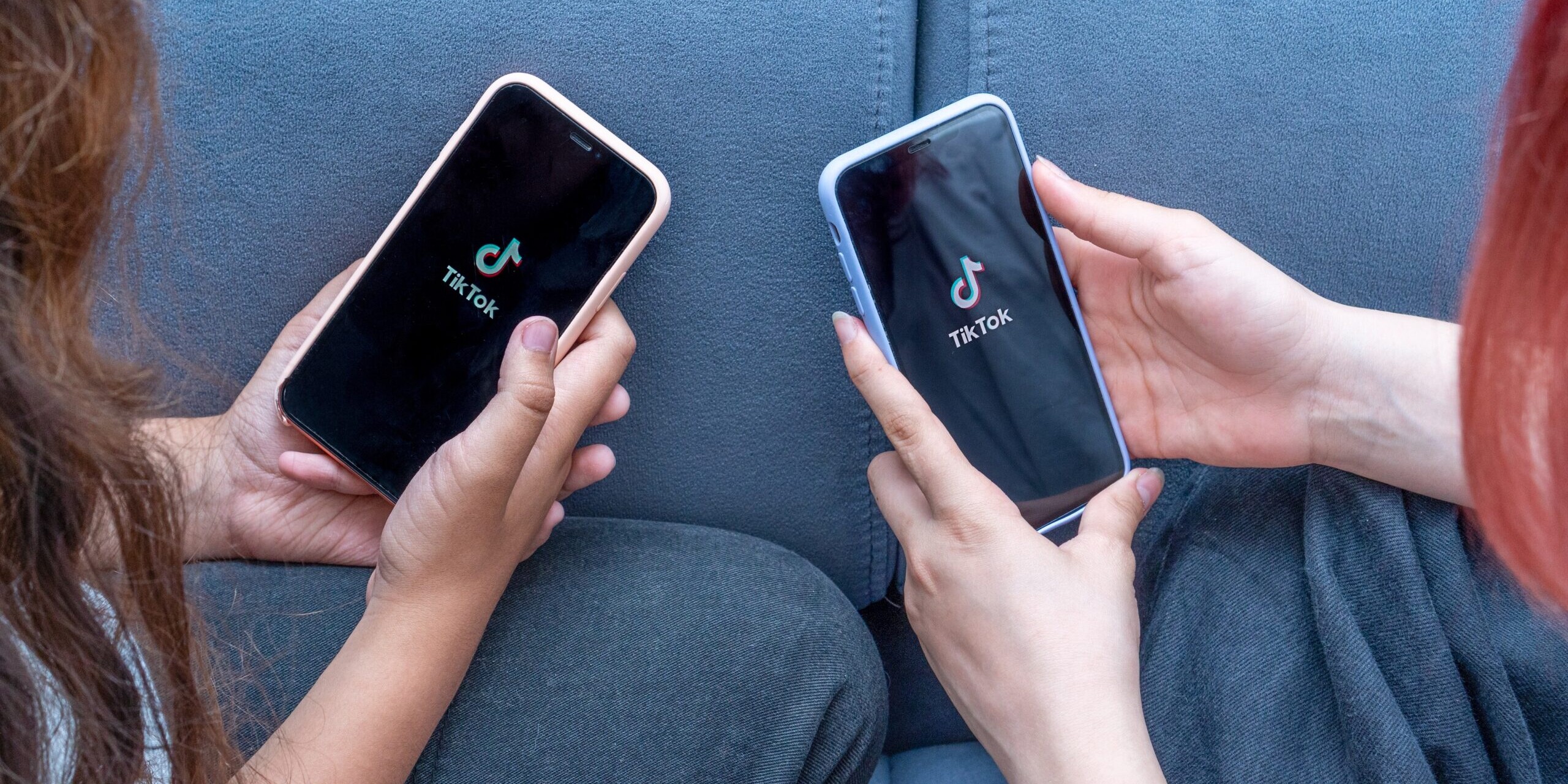 Two teenage girls with phones in their hands are sitting at home on bed. Social Media tiktok is loaded on screen.