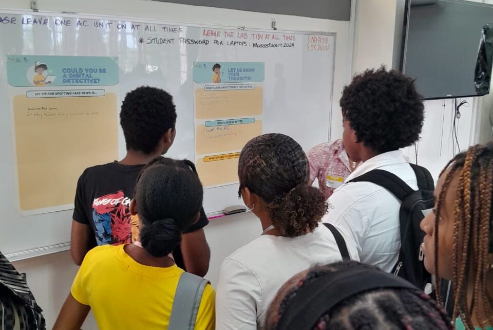 A group of students huddled around a whiteboard with pens.