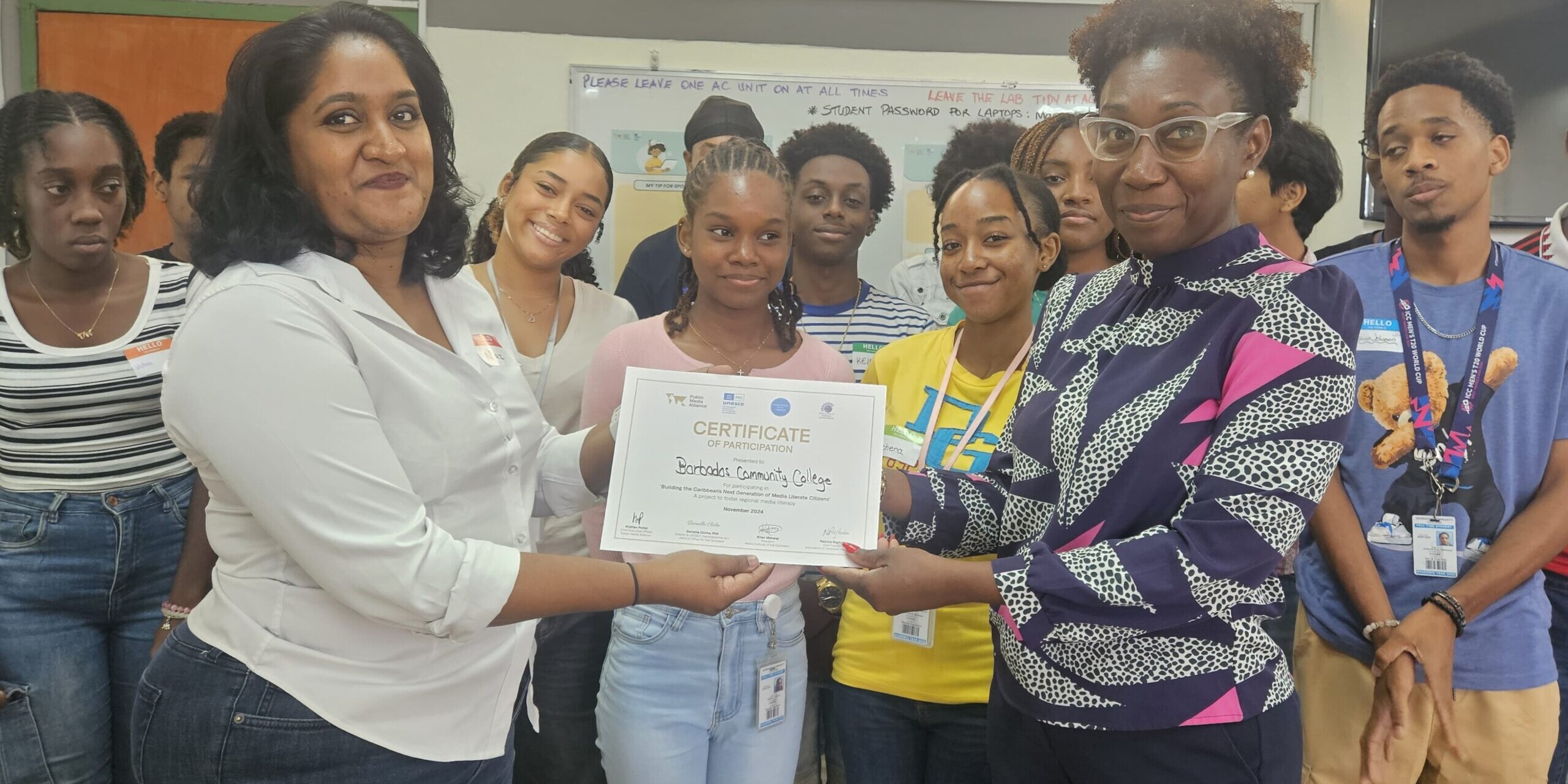 Facilitator Nazima Raghubir presents a certificate of participation to the Barbados Community College following a media literacy assembly with students on 5 November. Wendy Cox, Senior Tutor (Ag) within the Division of General And Continuing Education (foreground, right) receives the certificate while students watch on.