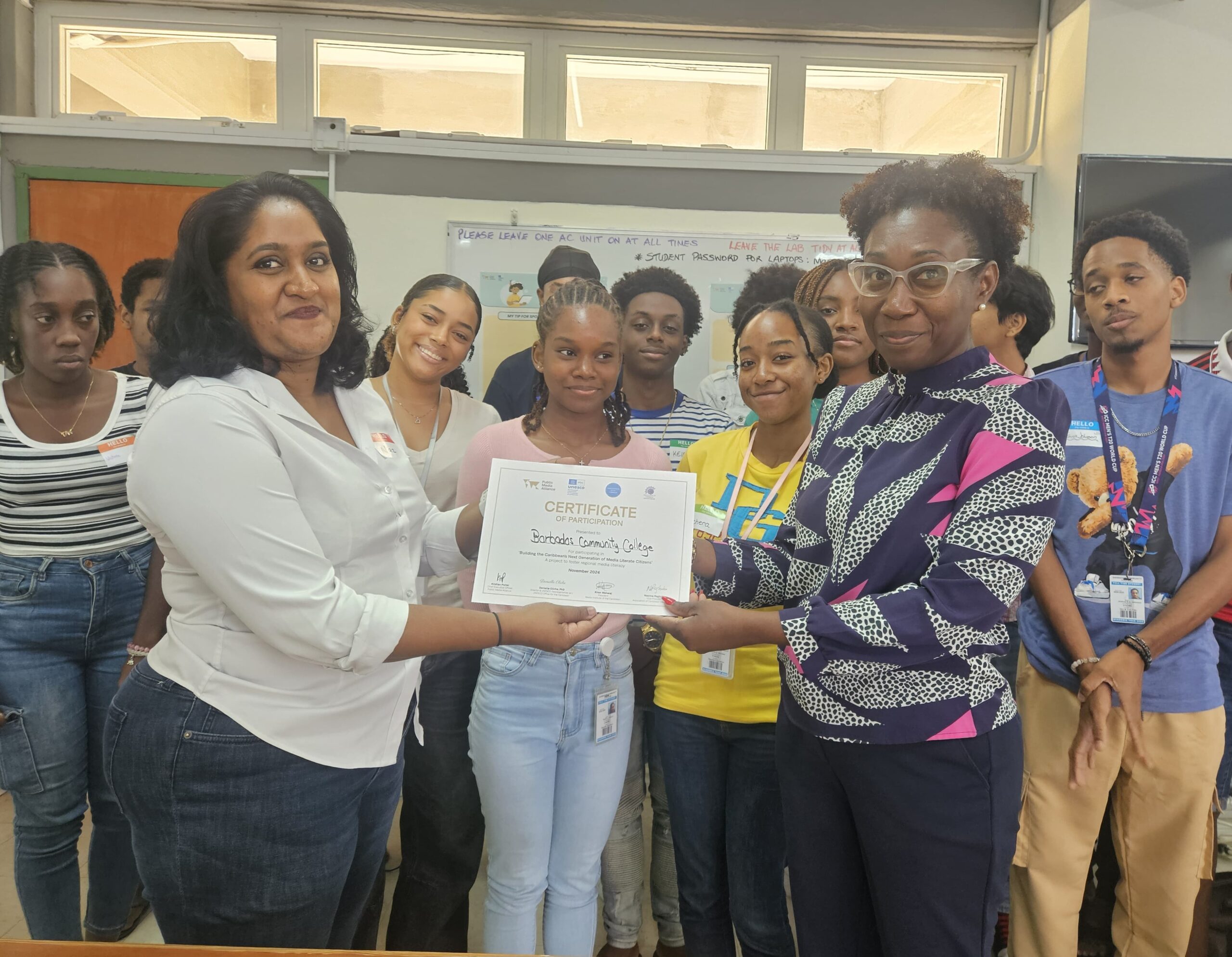 Facilitator Nazima Raghubir presents a certificate of participation to the Barbados Community College following a media literacy assembly with students on 5 November. Wendy Cox, Senior Tutor (Ag) within the Division of General And Continuing Education (foreground, right) receives the certificate while students watch on.